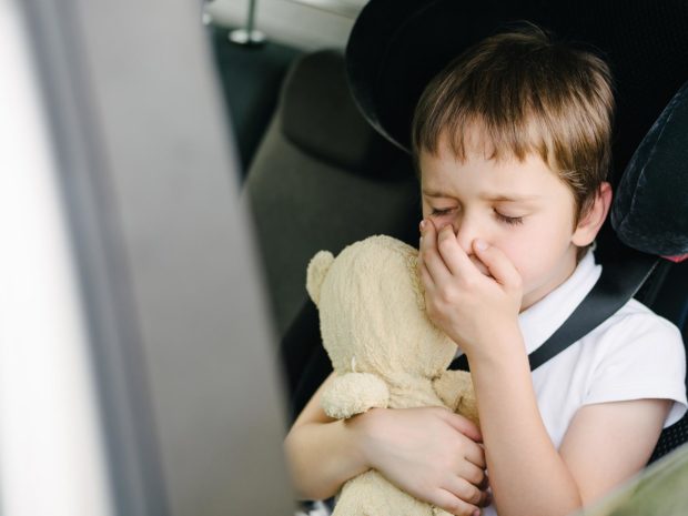 bambino in macchina con mano davanti alla bocca abbracciato al suo orso di peluche