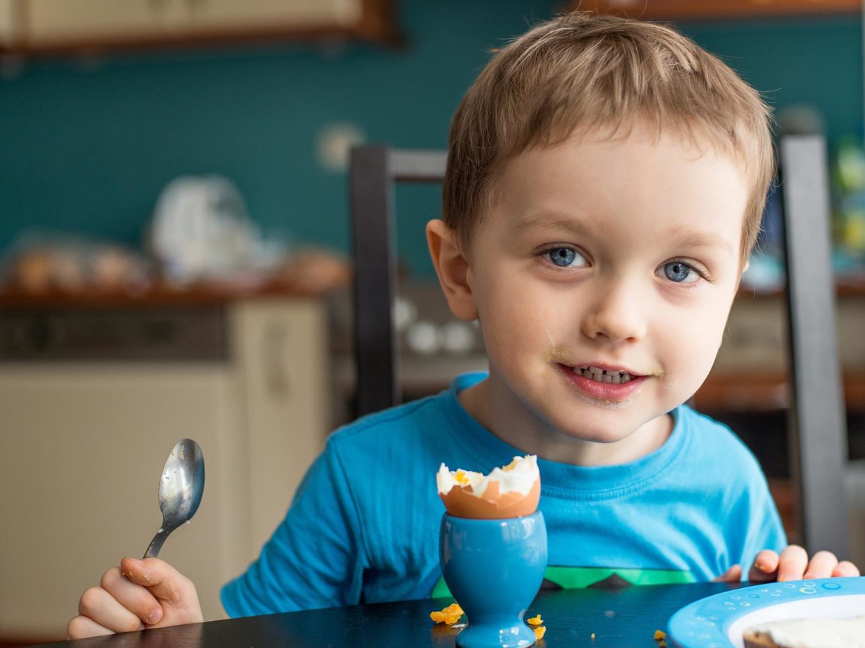 bambino sorridente mangia uovo alla coque