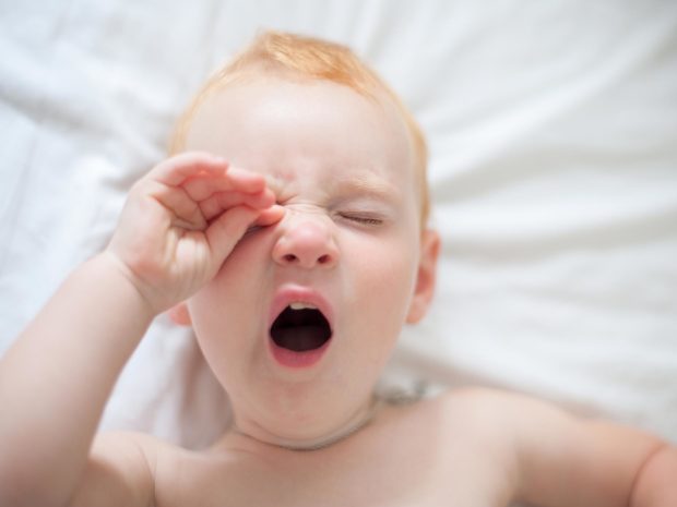 bambino con i capelli rossi sbadiglia toccandosi l'occhio