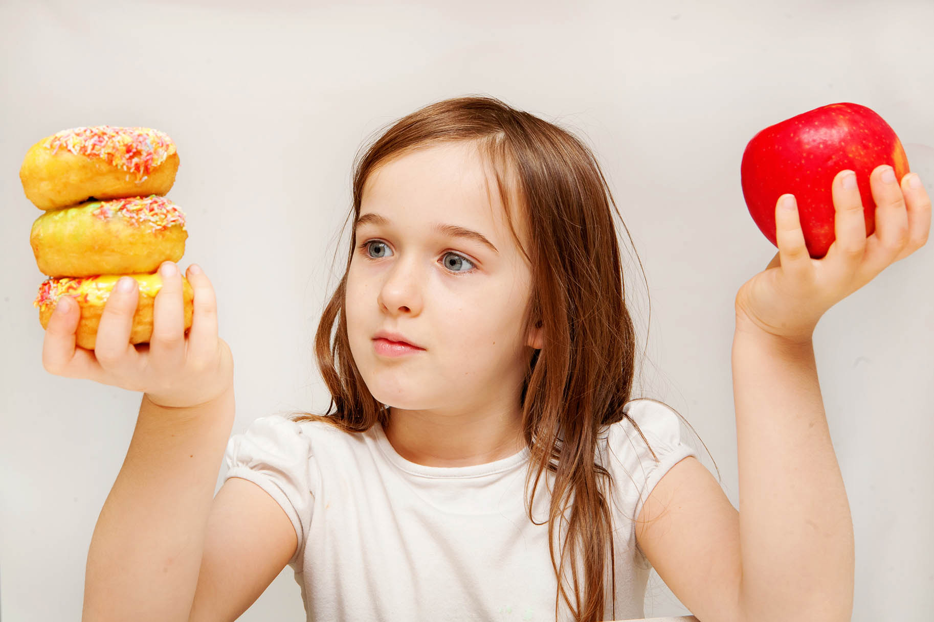 bambina con in mano da un lato una mela dall'altro delle ciambelle