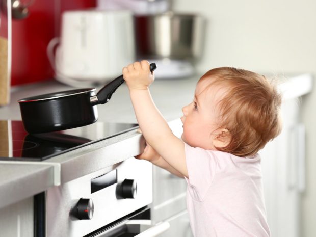 bambino prova a sollevare il pentolino dal piano cottura