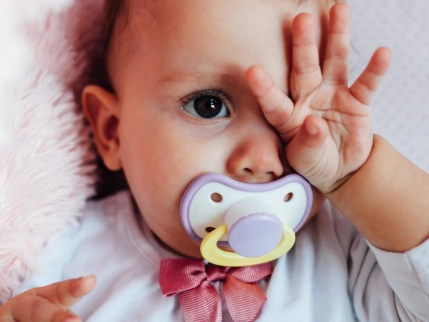 neonato con ciuccio si tocca con la mano l'occhio