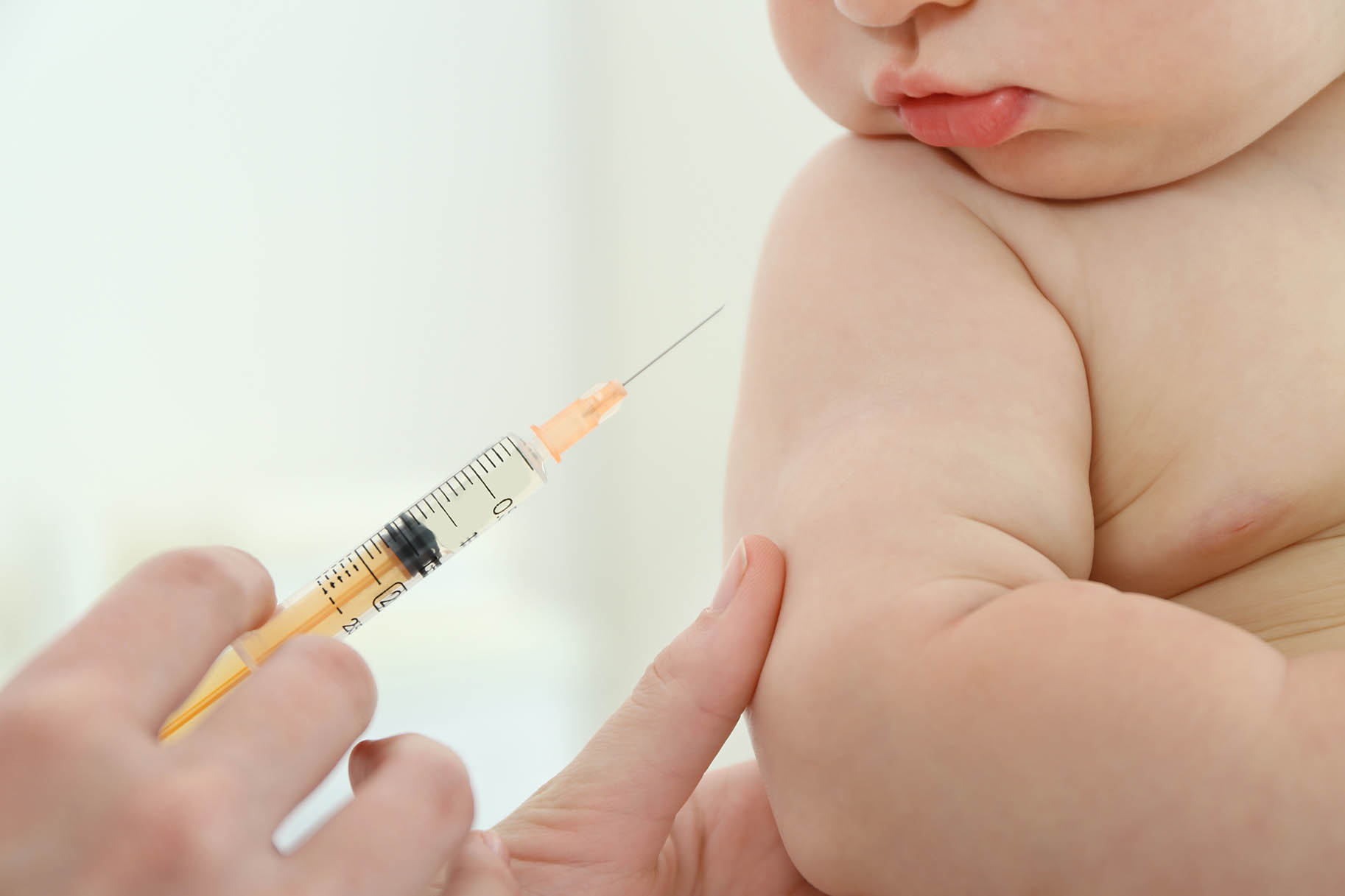 braccio di un neonato con accanto siringa pronta per la vaccinazione