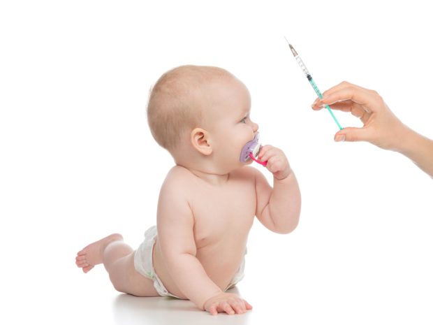 neonato su sfondo bianco guarda curioso mano che tiene una siringa