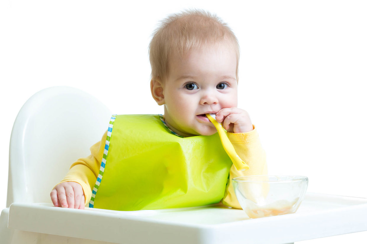 bambino sul seggiolone con cucchiaino in bocca