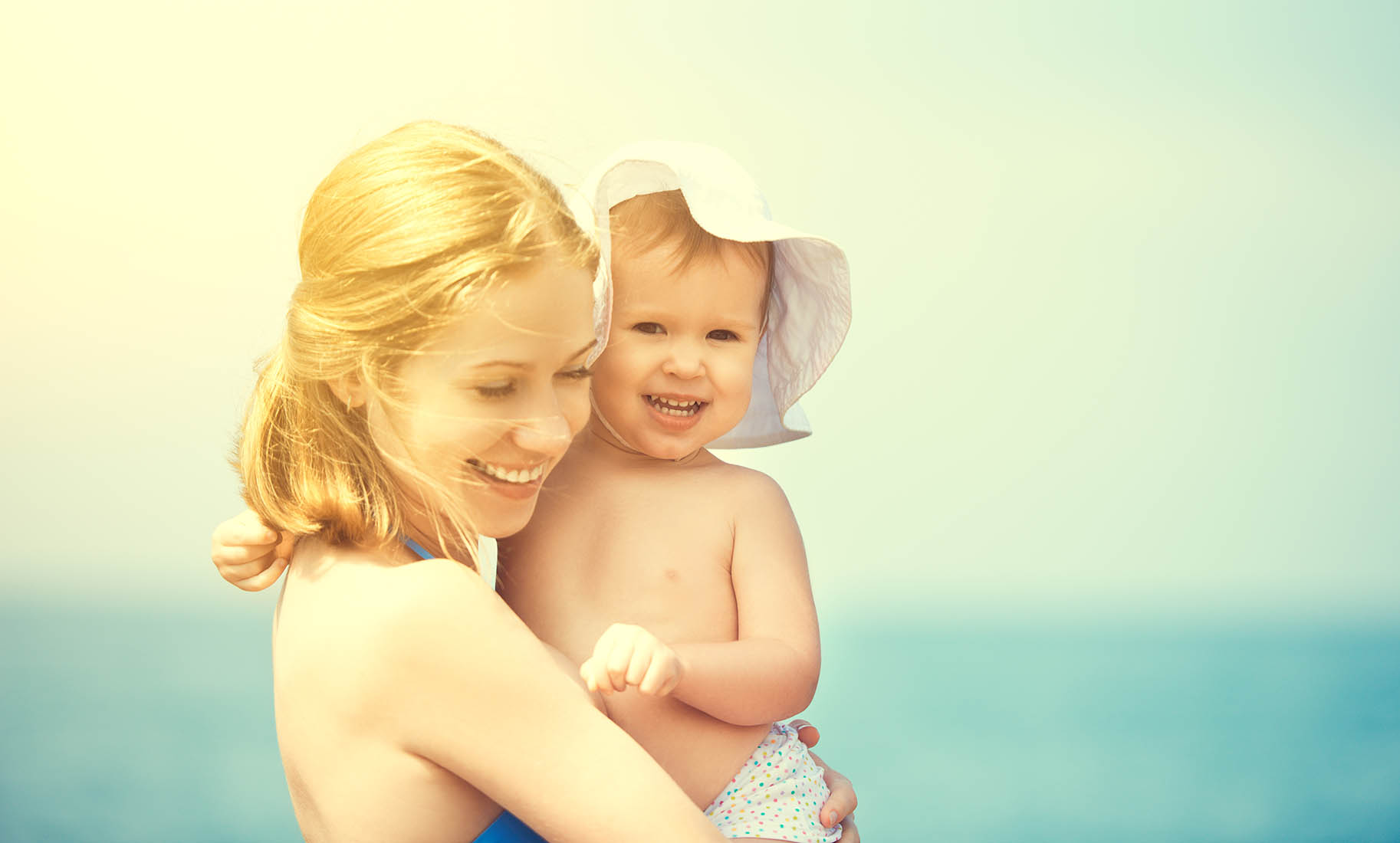 mamma con in braccio la figlia che indossa cappello per il sole