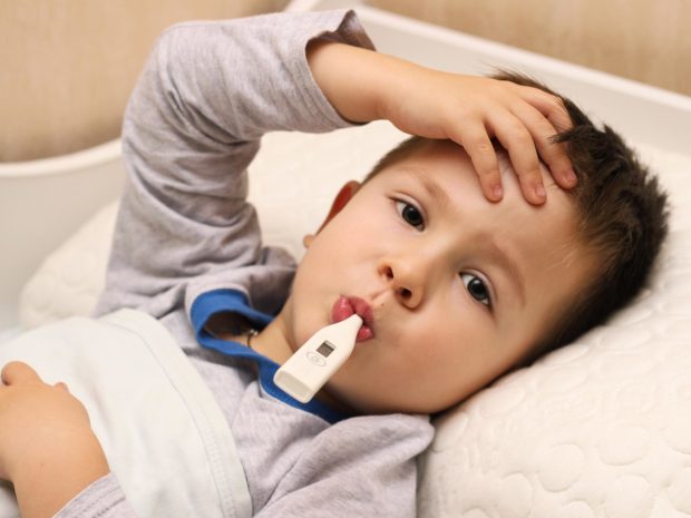 bambino con termometro in bocca si tocca la fronte