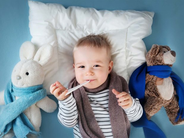 bambino disteso a letto con termometro alla bocca
