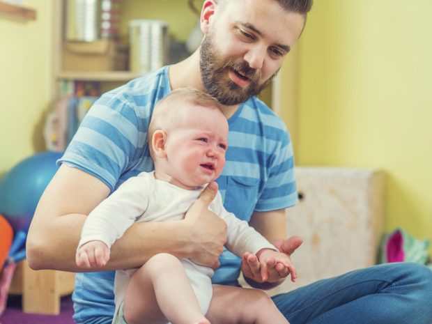 neonato piange tra le braccia del padre che prova a consolarlo