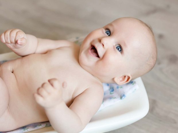neonato sorridente disteso sulla bilancio per essere pesato