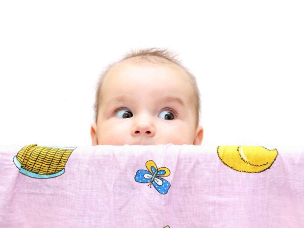 bambino spunta da dietro una coperta rosa con disegni