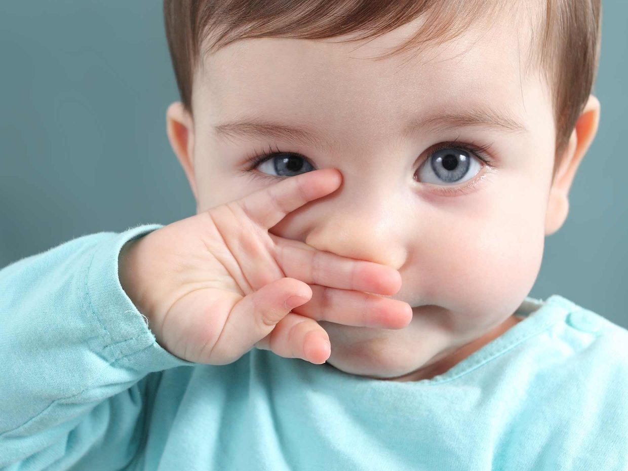 bambino con maglietta azzurra si gratta il naso con la mano