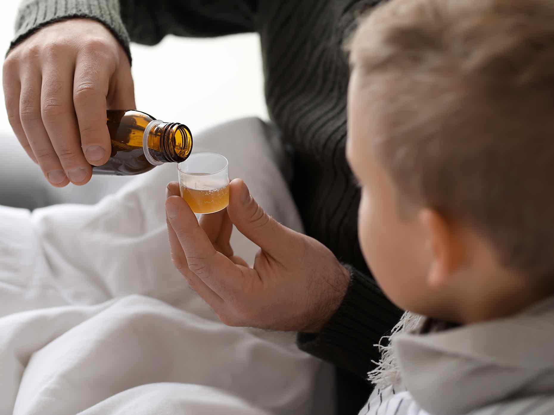 Father giving medicine to his son ill with flu at home