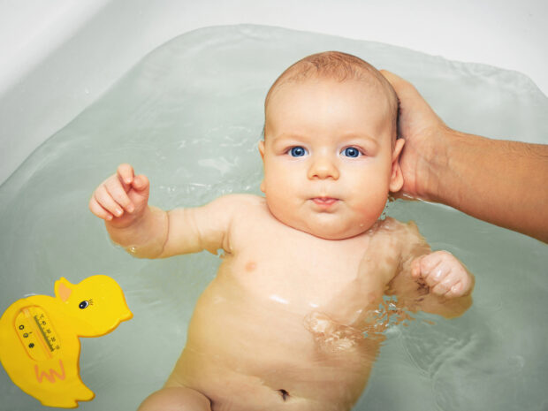 Mamma che lava un neonato usando un termometro per misurare la temperatura dell'acqua del bagnetto