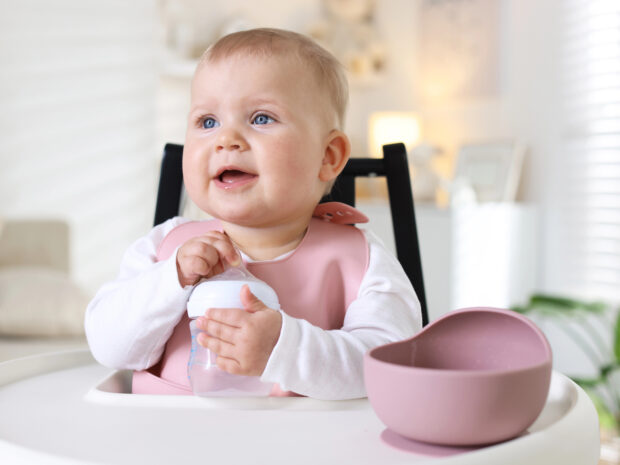 Bimba sul seggiolone con piattino per la pappa e biberon vuoto in mano